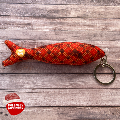 Chaveiro de sardinha em tecido vermelho com padrão xadrez, anel metálico, sobre fundo de madeira cinza