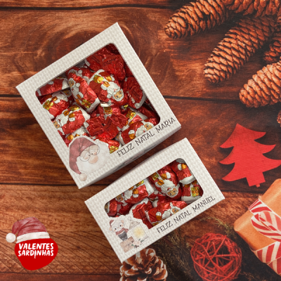 Caixas de chocolates natalícios embrulhados em papel vermelho, com mensagens personalizadas, sobre fundo de madeira decorado.