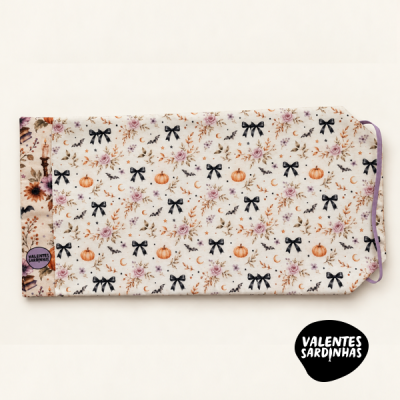 Capa de tecido com padrão floral, abóboras, laços e morcegos com etiqueta Valentes Sardinhas