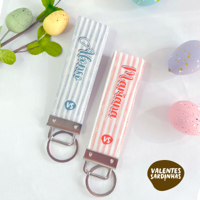 Dois porta-chaves de tecido às riscas azul e rosa com nomes e argolas metálicas, ovos decorativos e logo Valentes Sardinhas