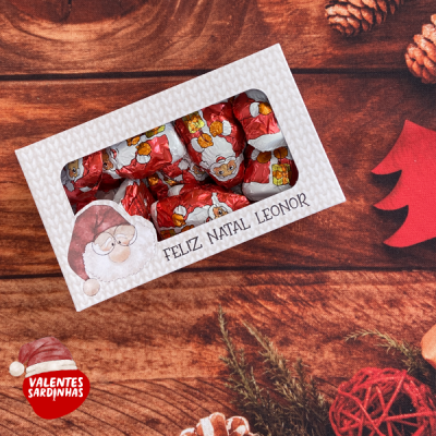 Caixa branca com chocolates embrulhados em papel vermelho com imagens de Pai Natal, texto 'FELIZ NATAL LEONOR'
