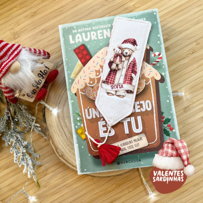 Marcador de livros com ursinho pijama vermelho sobre livro verde e decoração natalícia