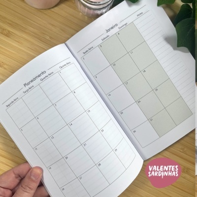 Livro de planejamento mensal aberto numa mesa de madeira com vela e planta