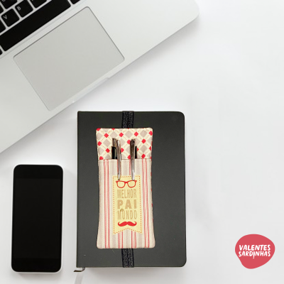 Estojo de tecido com canetas e marcador de livro sobre caderno preto ao lado de smartphone e portátil