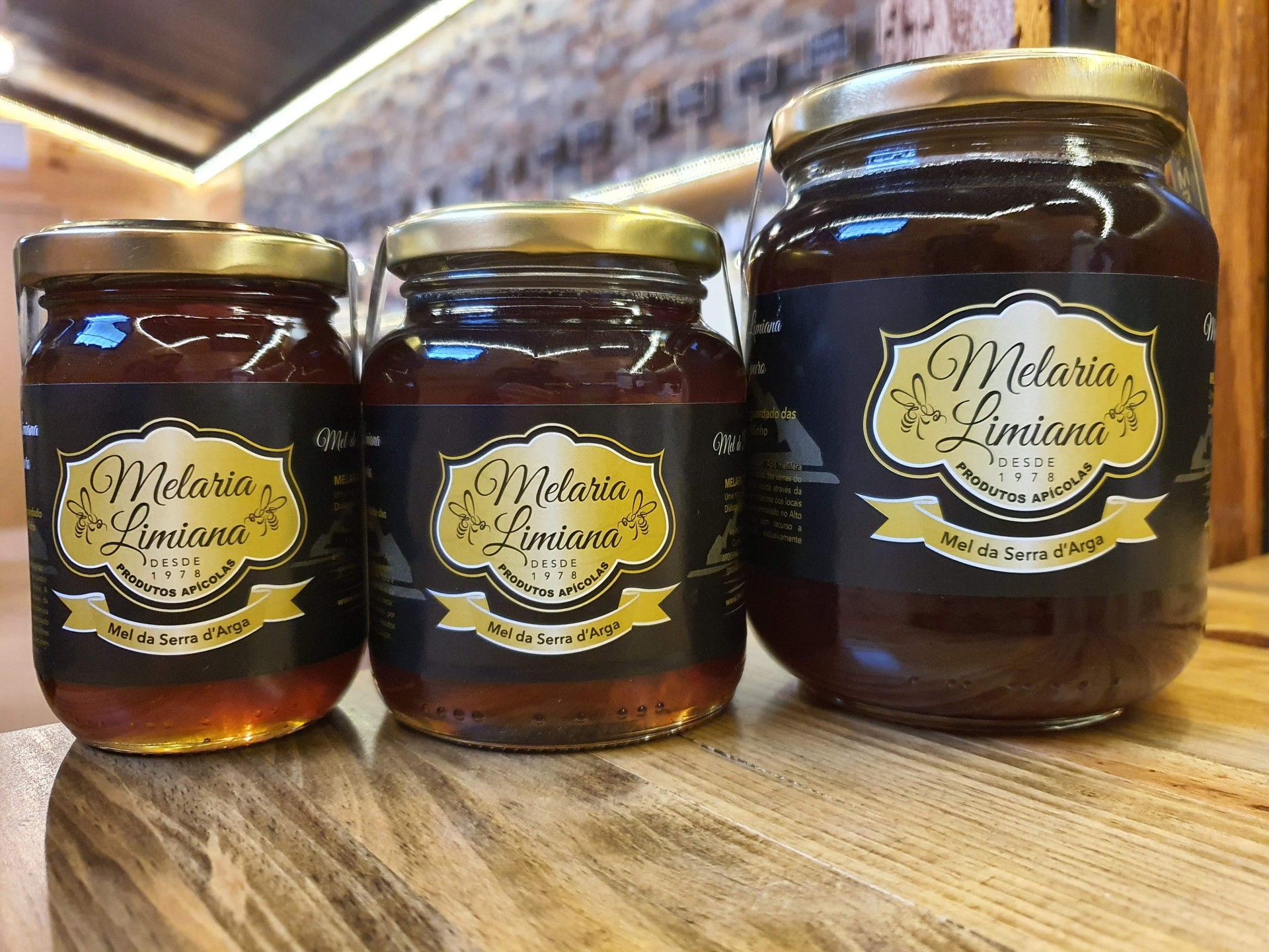 Mel da Serra d'Arga Três frascos de mel Melaria Limiana sobre mesa de madeira