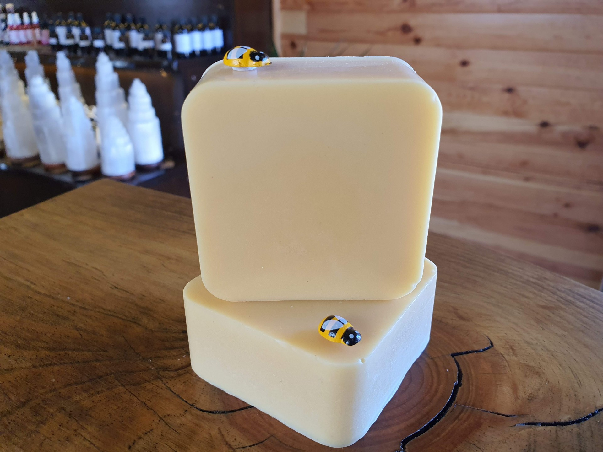 Sabonete Cera de Abelha Sabonetes quadrados creme com pequenos adornos de abelhas em cima, sobre mesa de madeira