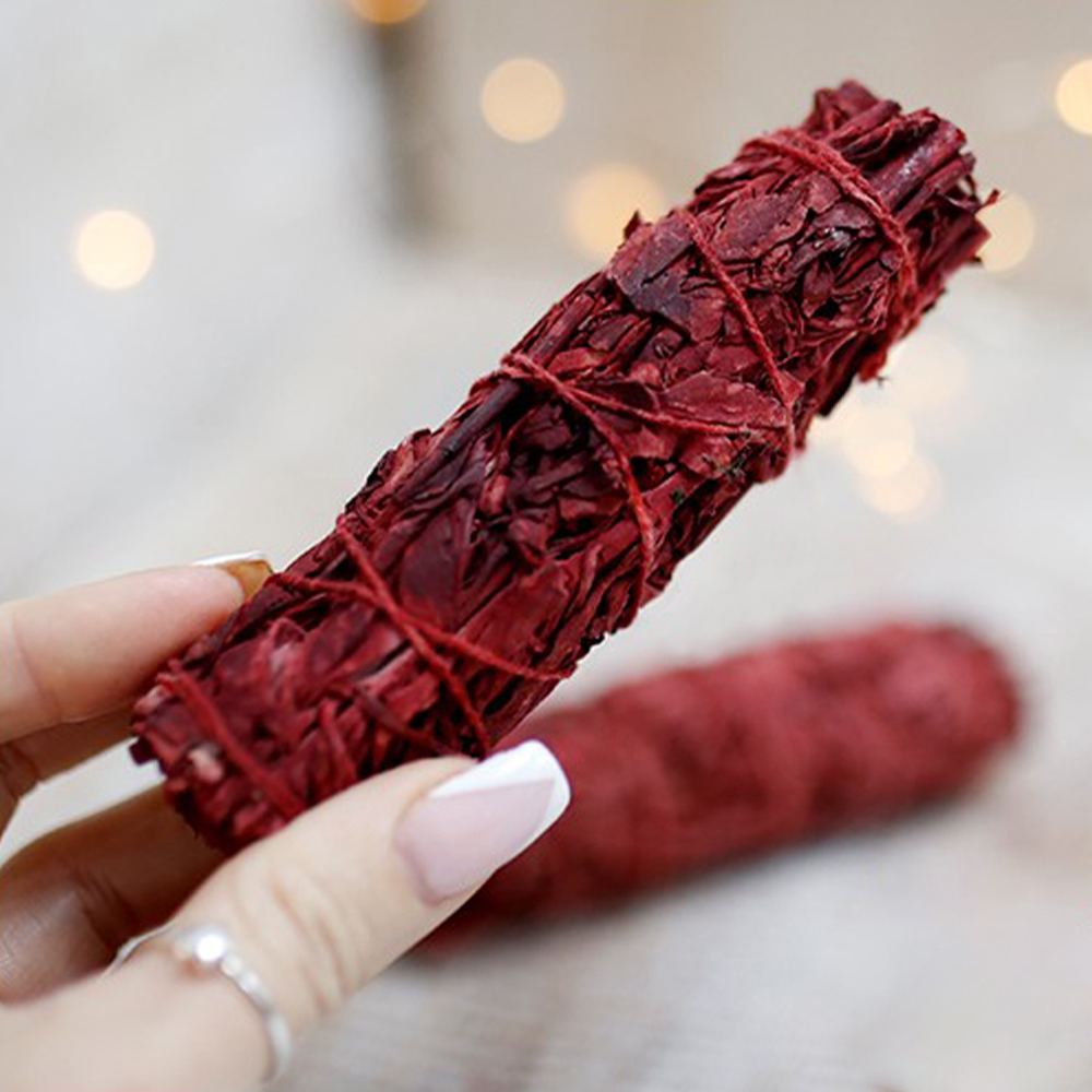 Tocha Purificante - Sangue de Dragão Feixe vermelho de folhas secas amarradas segurado por mãos femininas com unhas pintadas