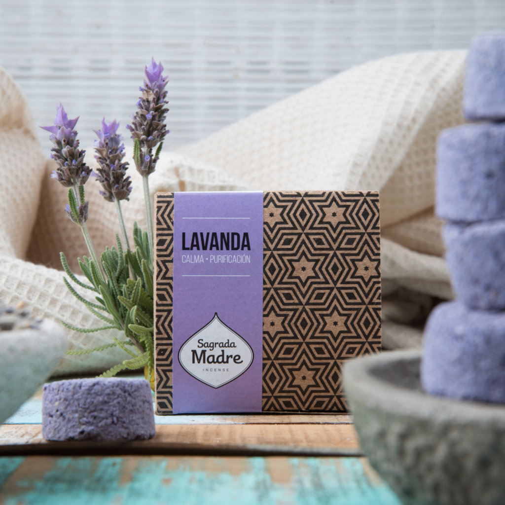 Pastilha Defumação Ativada Lavanda - Sagrada Madre Caixa de sabonete de lavanda da marca Sagrada Madre com flores naturais e sabonetes roxos empilhados em ambiente rústico