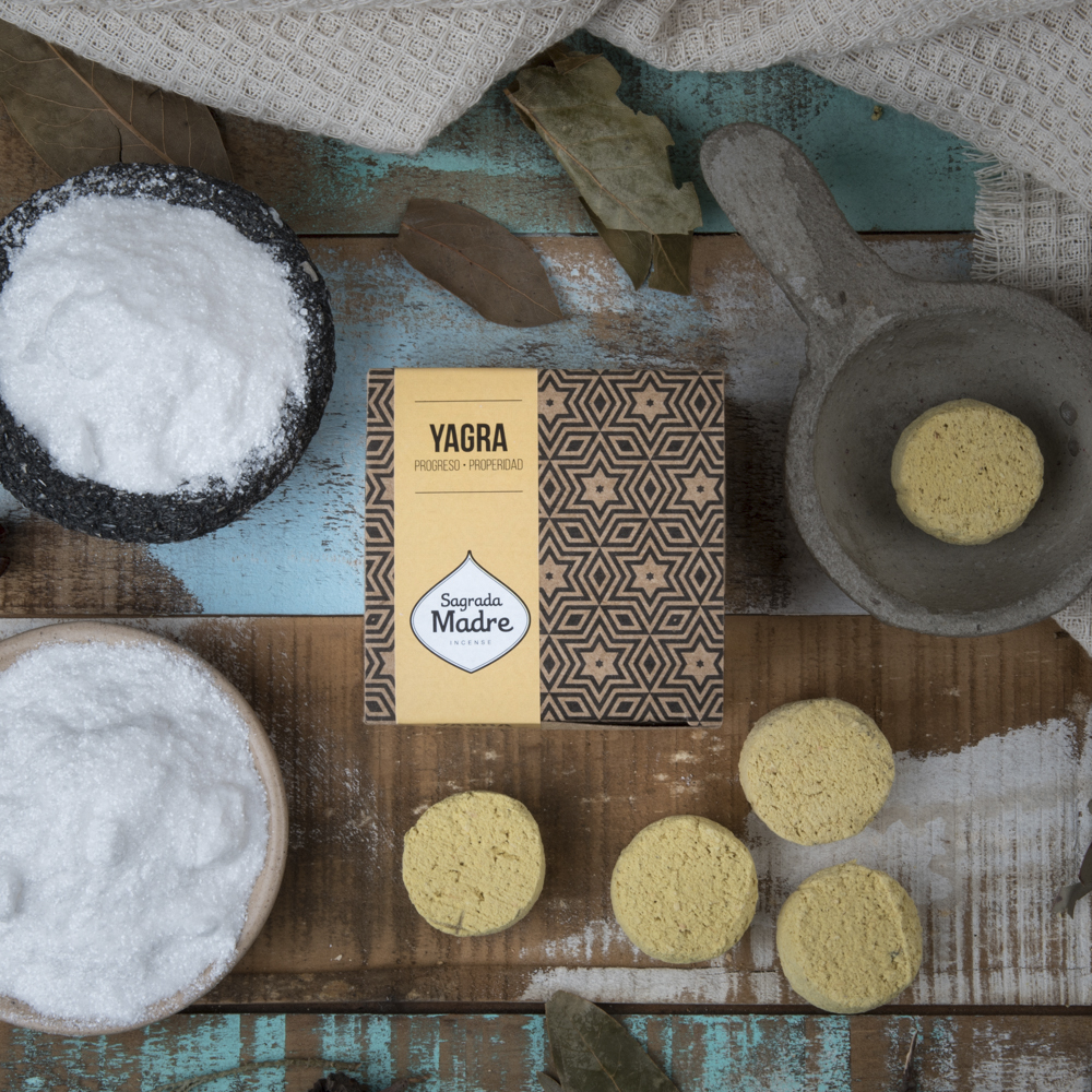 Pastilha Defumação Ativada Yagra - Sagrada Madre Produtos naturais com caixa YAGRA Sagrada Madre, sal grosso e pastilhas amarelas sobre mesa de madeira