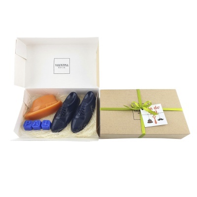 Caixa de chocolates com formato de sapatos castanhos e pretos, blocos azuis com letras P A D e embalagem com fita verde