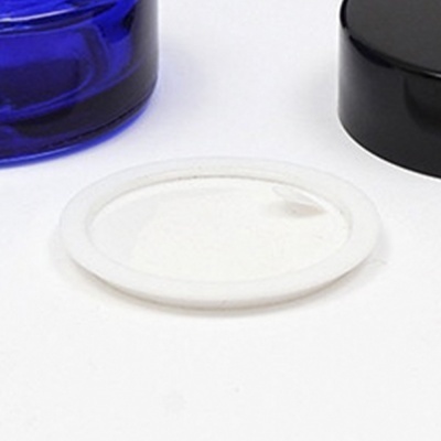 Tampa plástica branca entre frasco azul e tampa preta sobre superfície branca