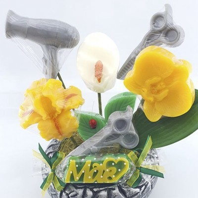 Arranjo artificial com flores amarelas e branca, utensílios de cozinha cinzentos e cartão 'Mãe' sobre base com folhas verdes