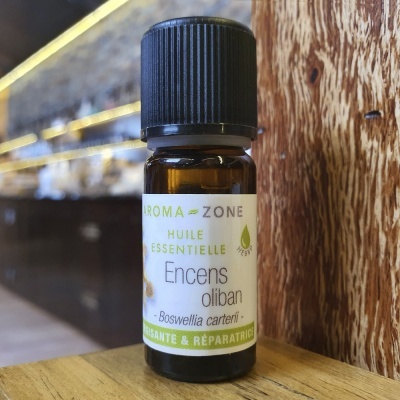 Frasco pequeno de óleo essencial de Incenso olíbano da Aroma-Zone com rótulo branco e verde sobre mesa de madeira e parede rústica