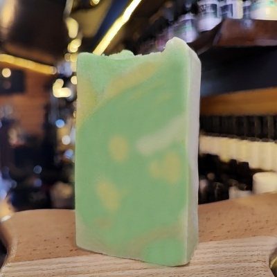 Sabonete artesanal verde e branco em barra sobre madeira com prateleiras ao fundo