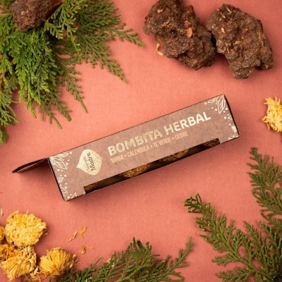 Caixa castanha de incenso herbal com folhas e flores secas ao redor sobre fundo rosa