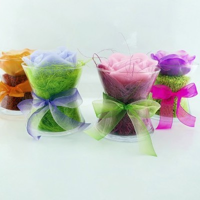 Velas decorativas em forma de rosa em copos transparentes com laços coloridos e musgo verde