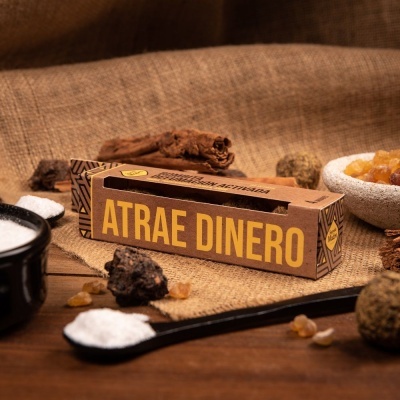 Caixa de incenso 'ATRAE DINERO' sobre mesa de madeira com elementos naturais ao redor