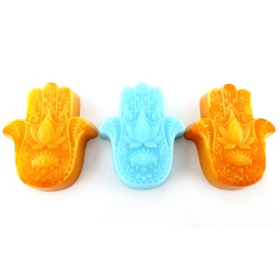 Três sabonetes em forma de mão Hamsá, dois laranja e um azul, com detalhes em relevo.