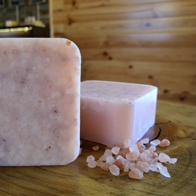 Dois sabonetes rosa claro quadrados com cristais de sal grosso rosa sobre superfície de madeira