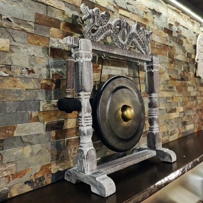 Gong decorativo em estrutura de madeira esculpida cinza numa mesa contra parede de pedras