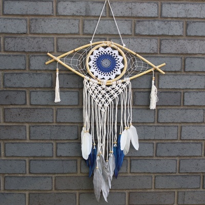 Apanhador de sonhos em formato de olho com penas e corda pendurado em parede de tijolos cinzentos