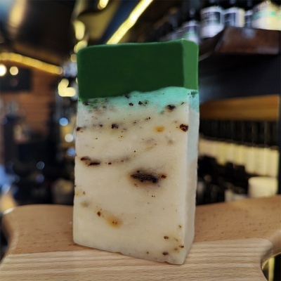Sabonete artesanal verde e branco com inclusões escuras sobre tábua de madeira