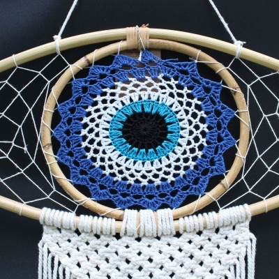Decoração de parede em forma de olho com crochê azul, branco, azul-turquesa e preto dentro de bambu circular.