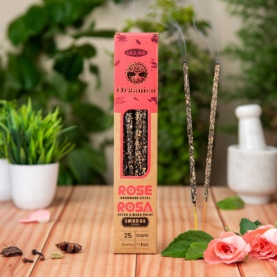 Caixa de incensos orgânicos com dois incensos acesos e flores rosas sobre mesa de madeira