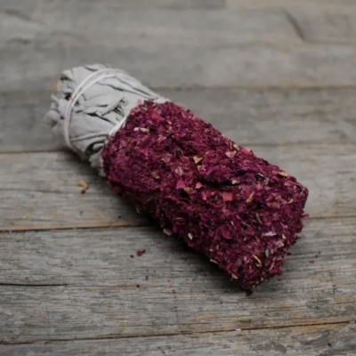 Vela artesanal branca coberta com folhas secas cor de rosa sobre madeira cinzenta