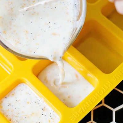 Mão a verter mistura cremosa em tabuleiro amarelo de moldes retangulares