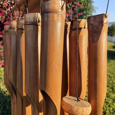 sinos de vento de bambu pendurados ao ar livre com vegetação e céu ao fundo
