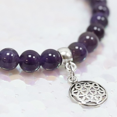 Pulseira de contas roxas com pendente prateado geométrico sobre fundo de lantejoulas brancas
