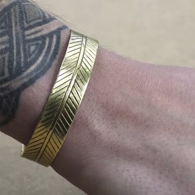 Pulseira dourada com padrão de linhas e tatuagem geométrica no pulso.