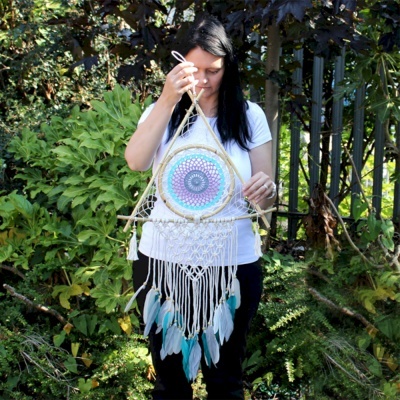 Mulher segurando apanhador de sonhos colorido com franjas e penas ao ar livre