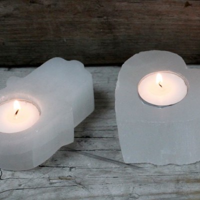 Dois porta-velas de pedra branca com velas acesas, em formas retangular e de coração, sobre madeira rústica.