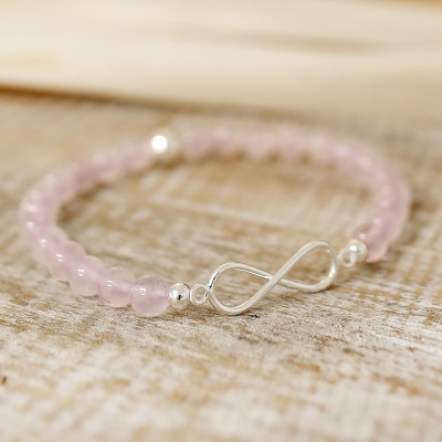 Pulseira rosa com fecho de infinito em metal prateado sobre superfície de madeira clara