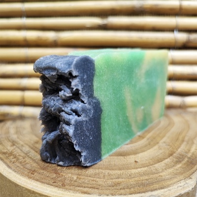 Barra de sabão verde e preta sobre madeira com fundo de bambu