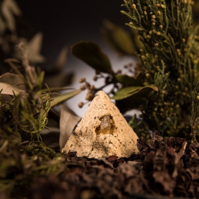 Peça piramidal bege clara entre sementes e folhas verdes