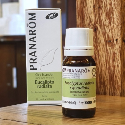 Frasco e caixa de óleo essencial de Eucalipto radiata da PRANARÔM sobre mesa de madeira.