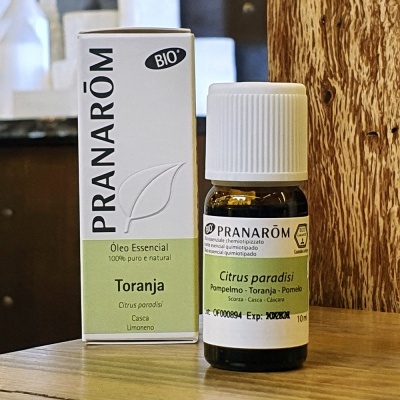 Frasco e caixa de óleo essencial Pranarôm Toranja com rótulos brancos e verdes sobre mesa de madeira