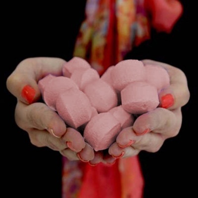 Várias pílulas cor-de-rosa seguradas por mãos femininas com unhas vermelhas