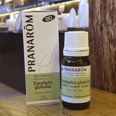 Frasco de óleo essencial Pranarôm Eucalipto globulus e caixa branca e verde em superfície de madeira.