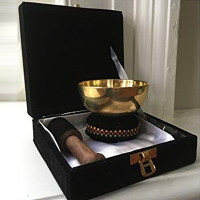 Taça tibetana dourada com suporte colorido e acessórios numa caixa preta forrada a branco