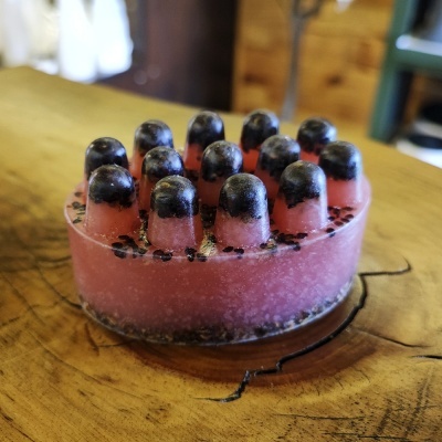 Sabonete redondo rosa com pontas pretas e sementes pretas sobre madeira clara