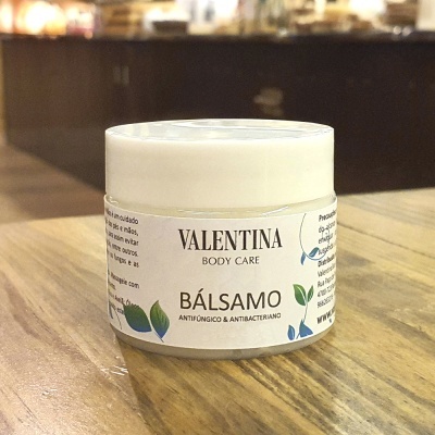 Pote branco de bálsamo antifúngico e antibacteriano Valentina Body Care sobre mesa de madeira
