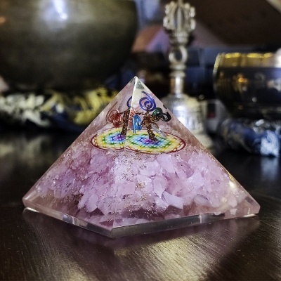 Pirâmide decorativa transparente com pedras roxas e símbolo colorido no topo