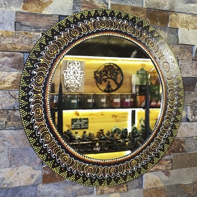 Espelho redondo com moldura decorativa em preto, amarelo, branco e laranja numa parede de pedra