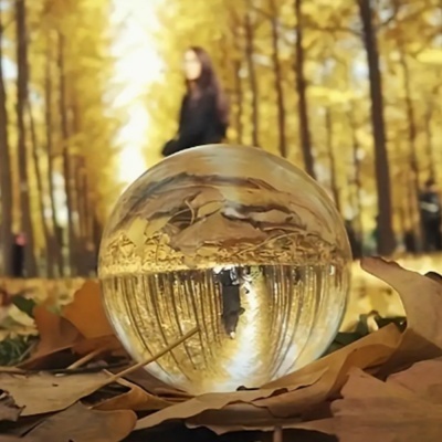 Esfera de vidro sobre folhas secas com floresta outonal e pessoa ao fundo desfocada