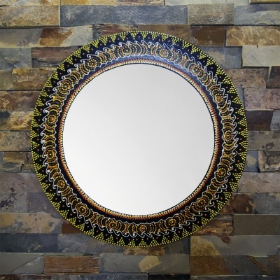 Espelho redondo com moldura colorida e parede de pedras ao fundo