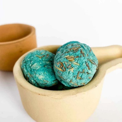 Bolas de banho azuis com partículas castanhas numa colher de cerâmica beige